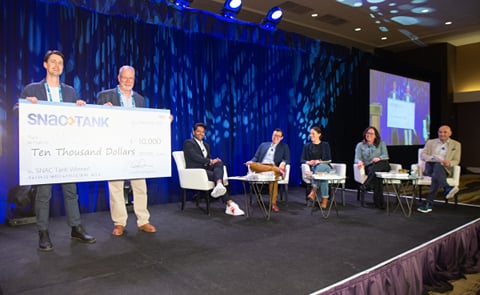 Candid snack company founder and CEO Chris Kajander receives the USD 10,000 grand prize for his pitch to SNAC Tank highlighting the sustainability of his company's Noons™ cacao bites snack Candid snack company founder and CEO Chris Kajander receives the USD 10,000 grand prize for his pitch to SNAC Tank highlighting the sustainability of his company's Noons™ cacao bites snack