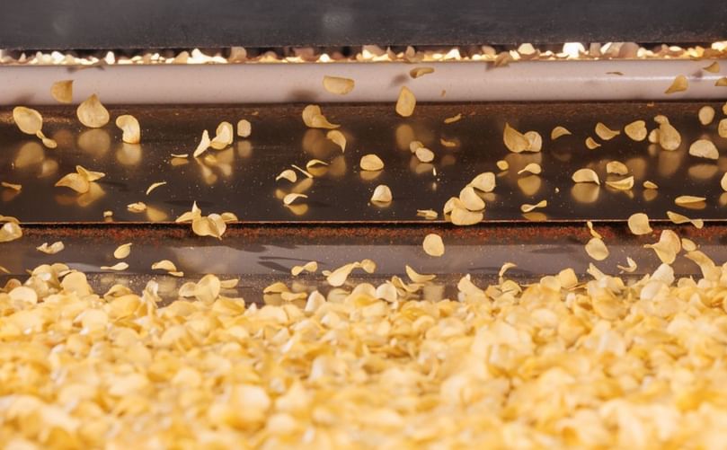Potato chips in motion on a processing line—minimizing surface moisture at this stage helps reduce frying energy consumption and improve efficiency.